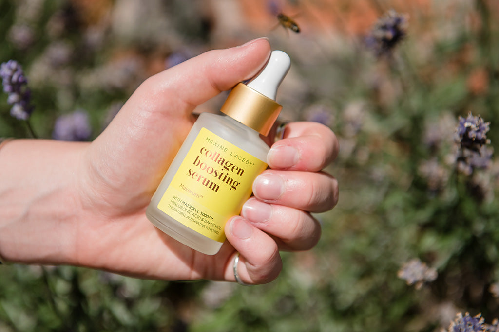 Photo of a white person's hand holding a bottle of Maxerum against a blurred green and grey background