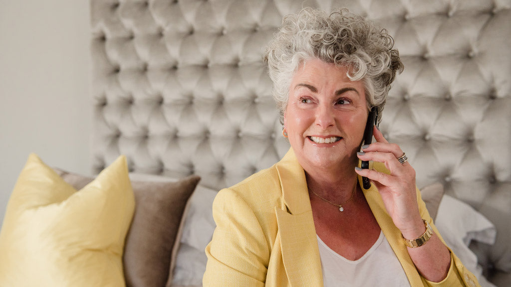 Photo showing Maxine Laceby sitting and smiling against a neutral background, she is wearing a white top and a yellow blazer