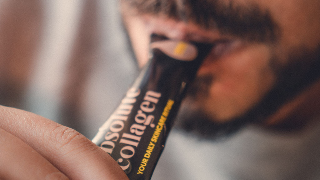 Close up photograph showing a tanned man with a dark beard taking an Absolute Collagen sachet